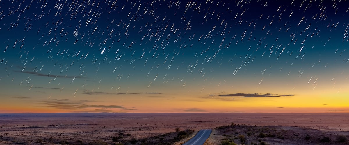 A starry night sky over a desert landscape with a winding road.