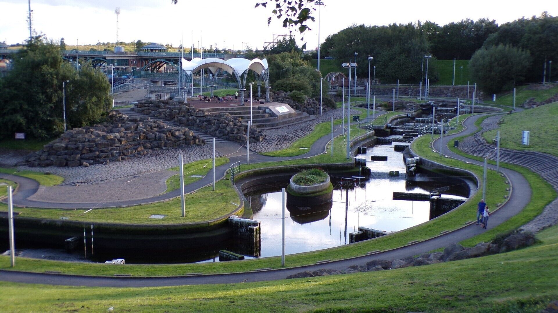 Um parque com lago, uma ponte e um edifício grande com cúpula.