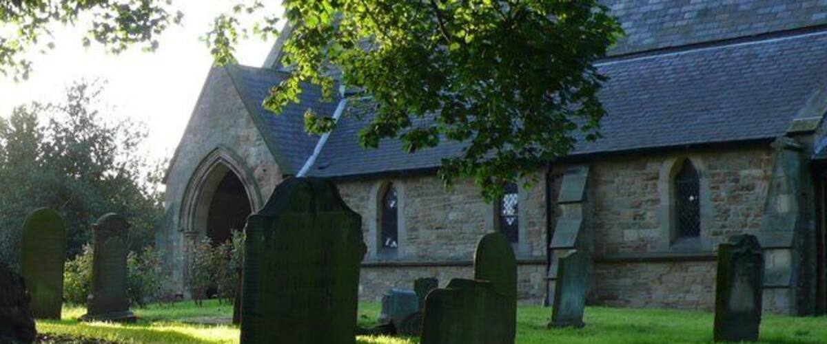A churchyard with stone headstones and a stone building with a pointed roof.