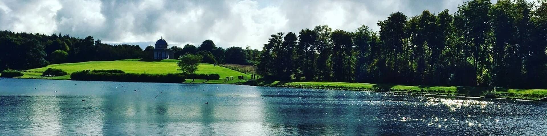 A lake surrounded by green fields and trees under a cloudy sky.