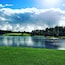 A lake surrounded by green fields and trees under a cloudy sky.