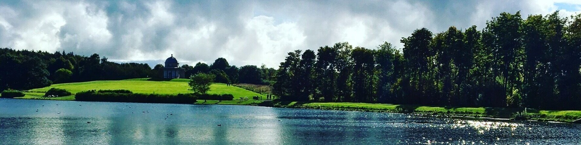 Um lago rodeado por campos verdes e árvores sob um céu nublado.