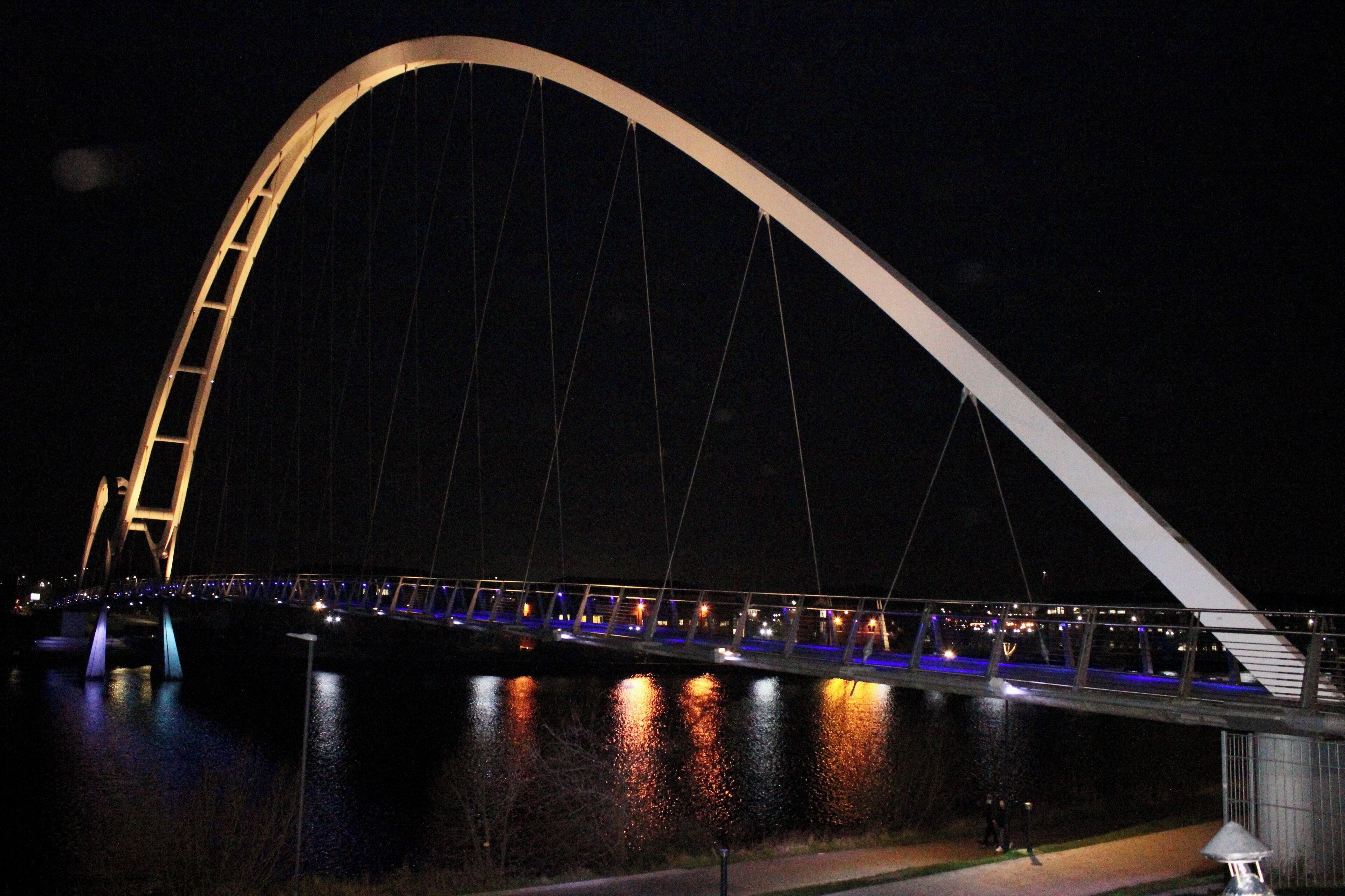 A large arched bridge at night with illuminated railings and a river below.