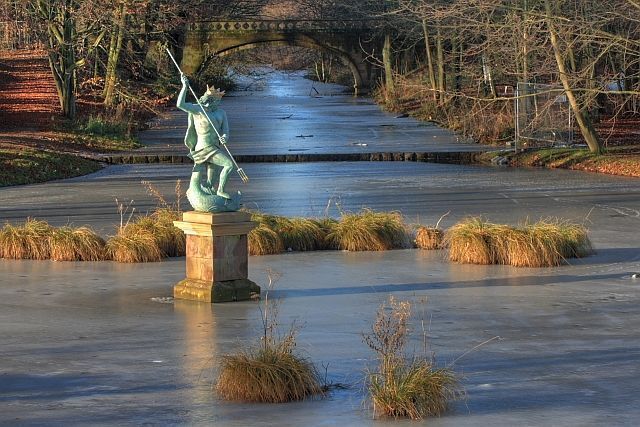 Statue of Neptune Guarding a bend in the frozen Serpentine Lake at Hardwick Hall Country Park. In the distance The Serpentine Bridge dating from 1754 and restored in 1994.
