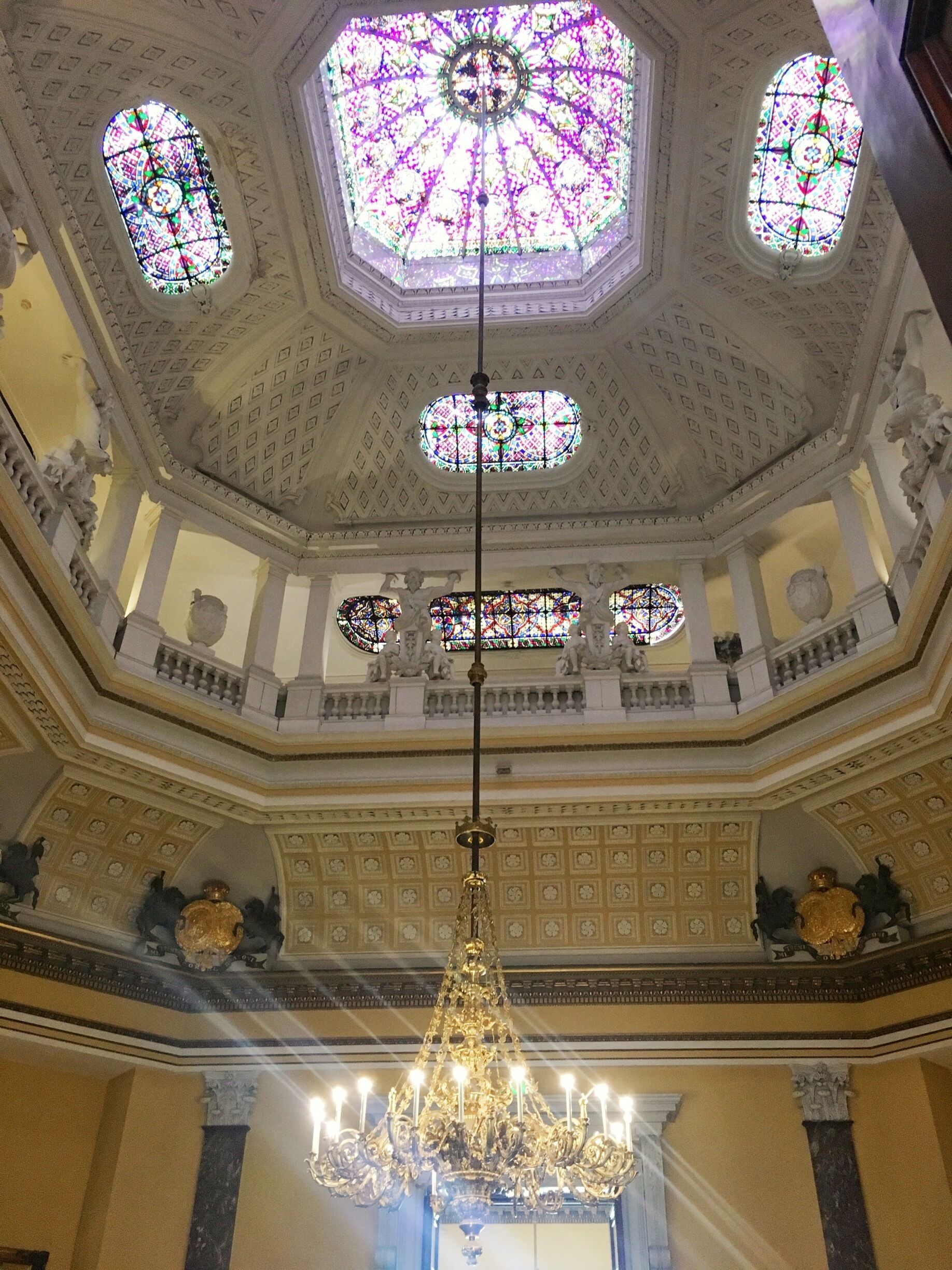 A grand hall with a high ceiling, ornate chandeliers, and stained glass windows.