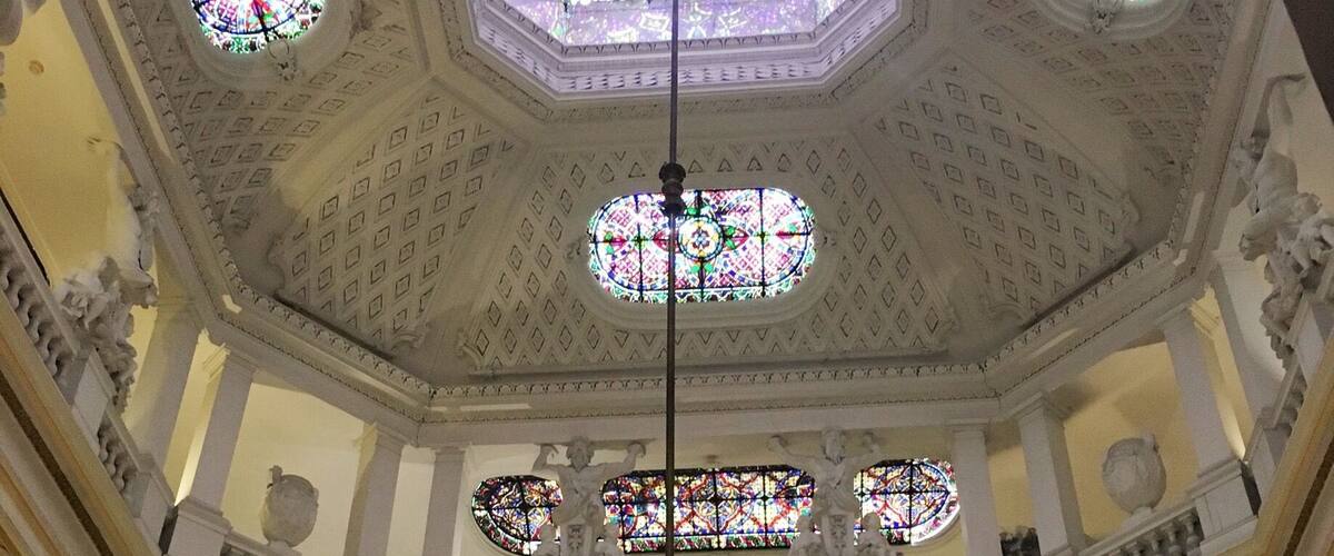 A grand hall with a high ceiling, ornate chandeliers, and stained glass windows.