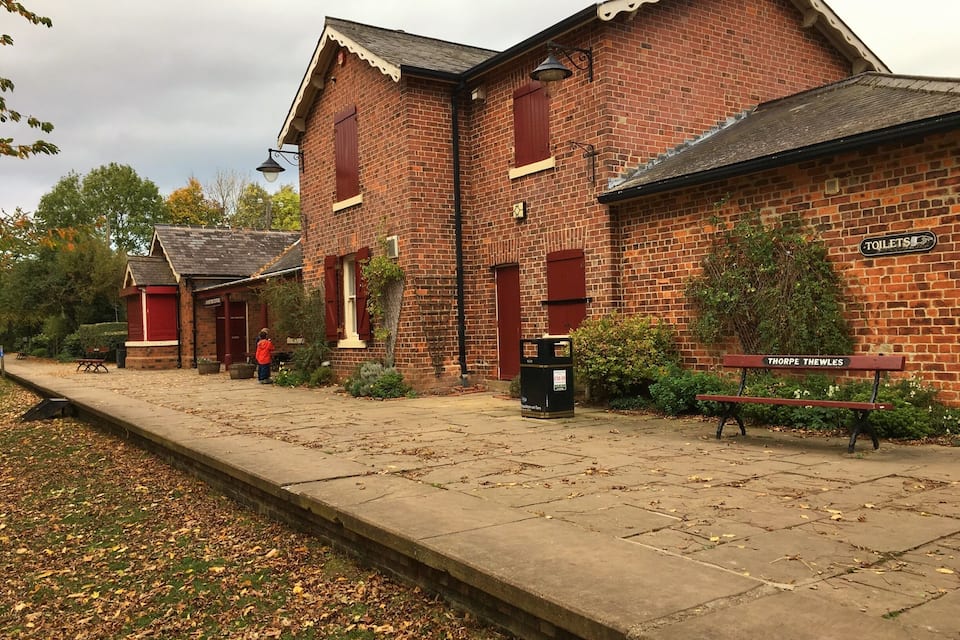 Een bakstenen gebouw met een bank waarop 'Thorpe Thewles' staat en een bordje voor toiletten.