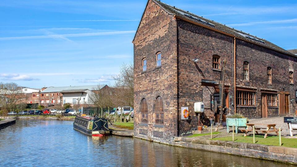A historic brick building by a canal with a narrowboat docked nearby.