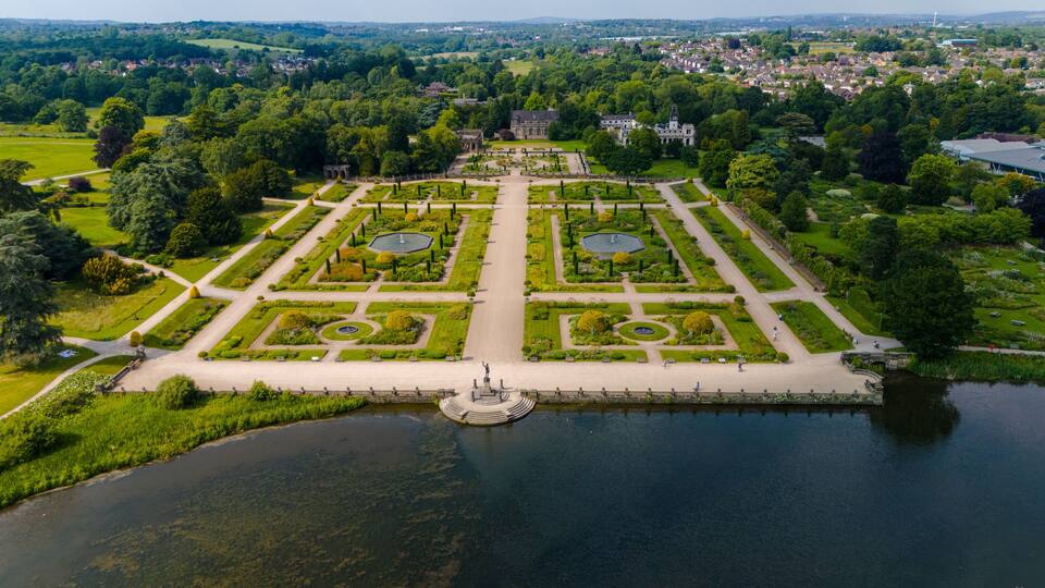 Vista aérea de un jardín formal con senderos simétricos, una fuente central y follaje circundante.