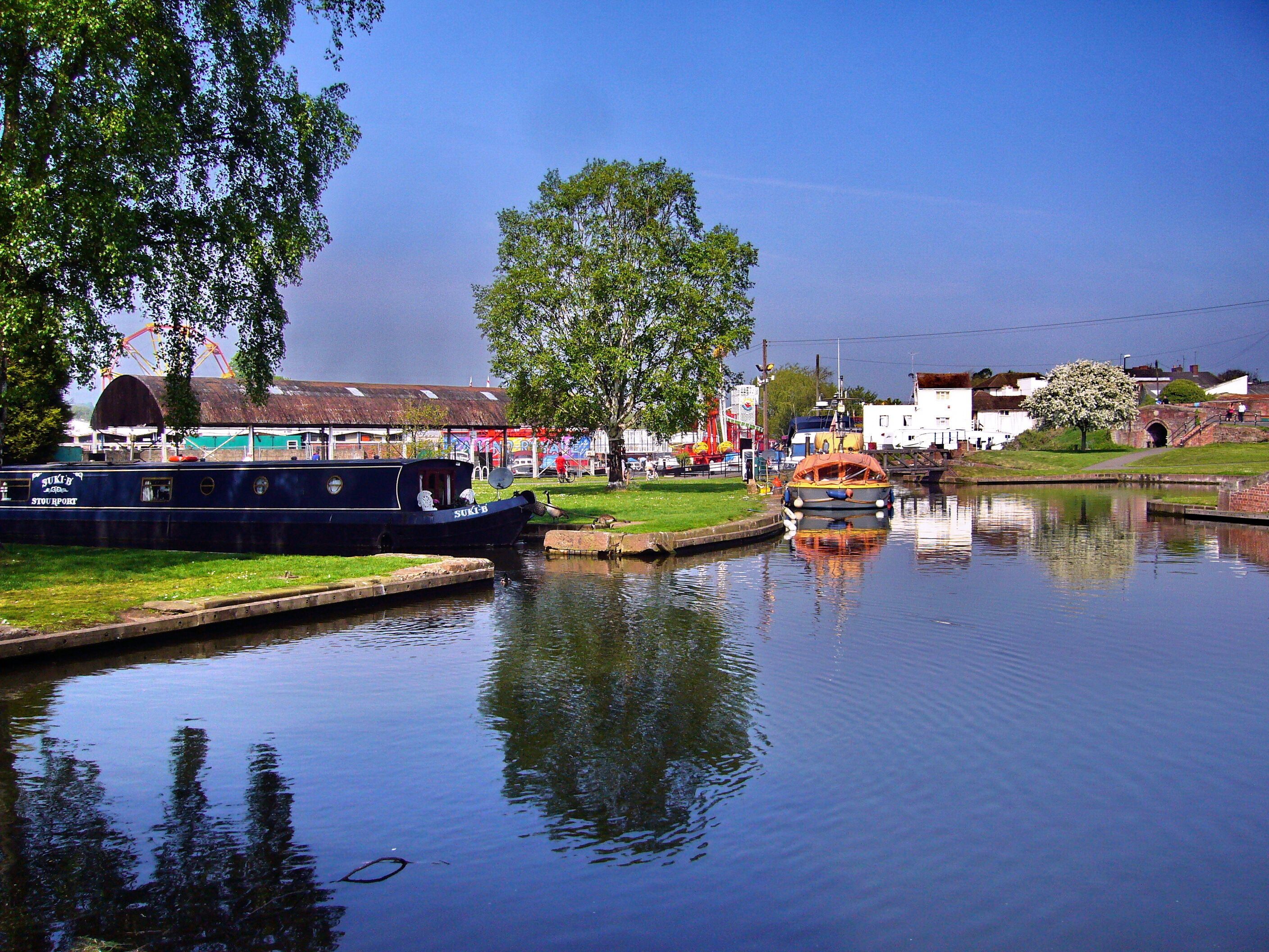 A calm river with boats, a tree, and buildings in the background.