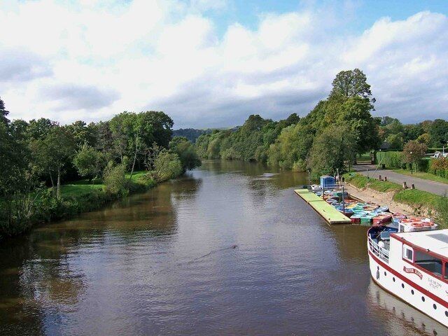 A river with a boat docked on the right, surrounded by greenery and trees.