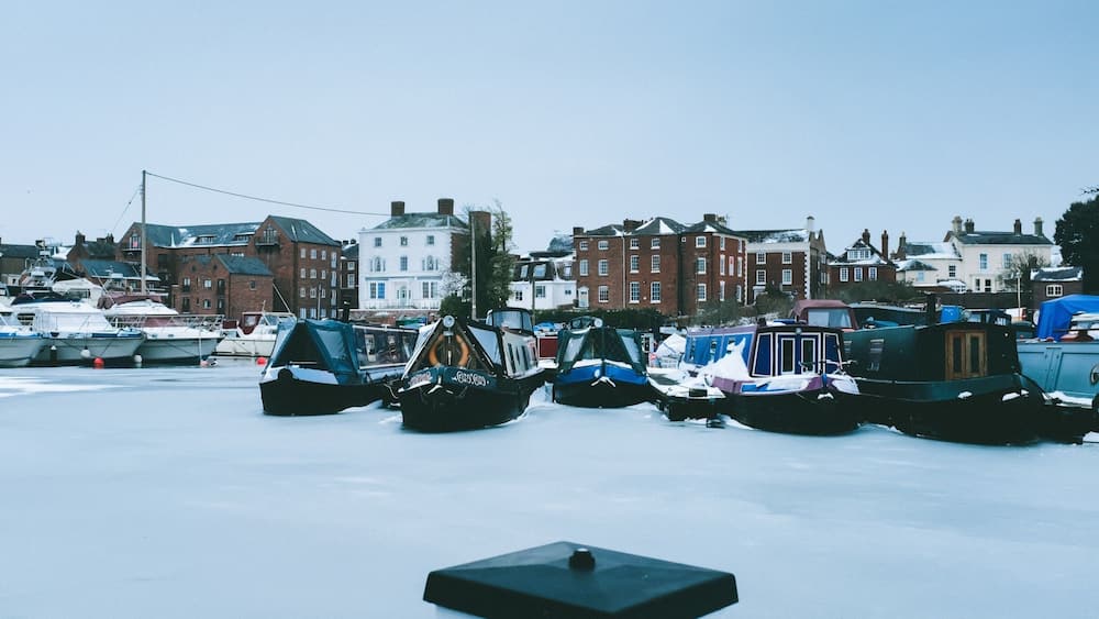 Un port de plaisance où des bateaux sont amarrés, le tout dans un décor enneigé et entouré de bâtiments historiques.