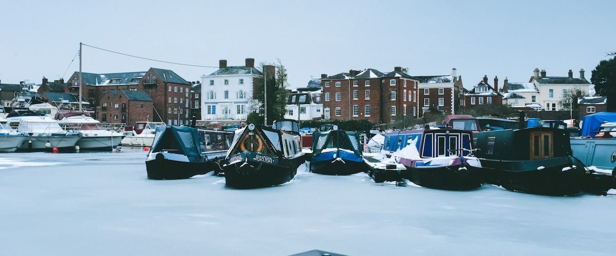 A marina with boats docked in a snowy setting, surrounded by historic buildings.