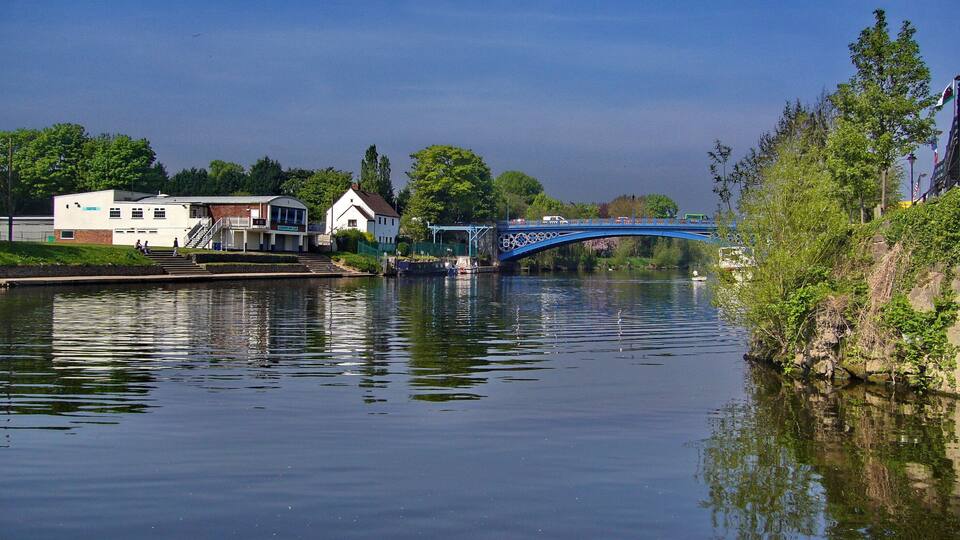 A river with a blue bridge, houses, and greenery.
