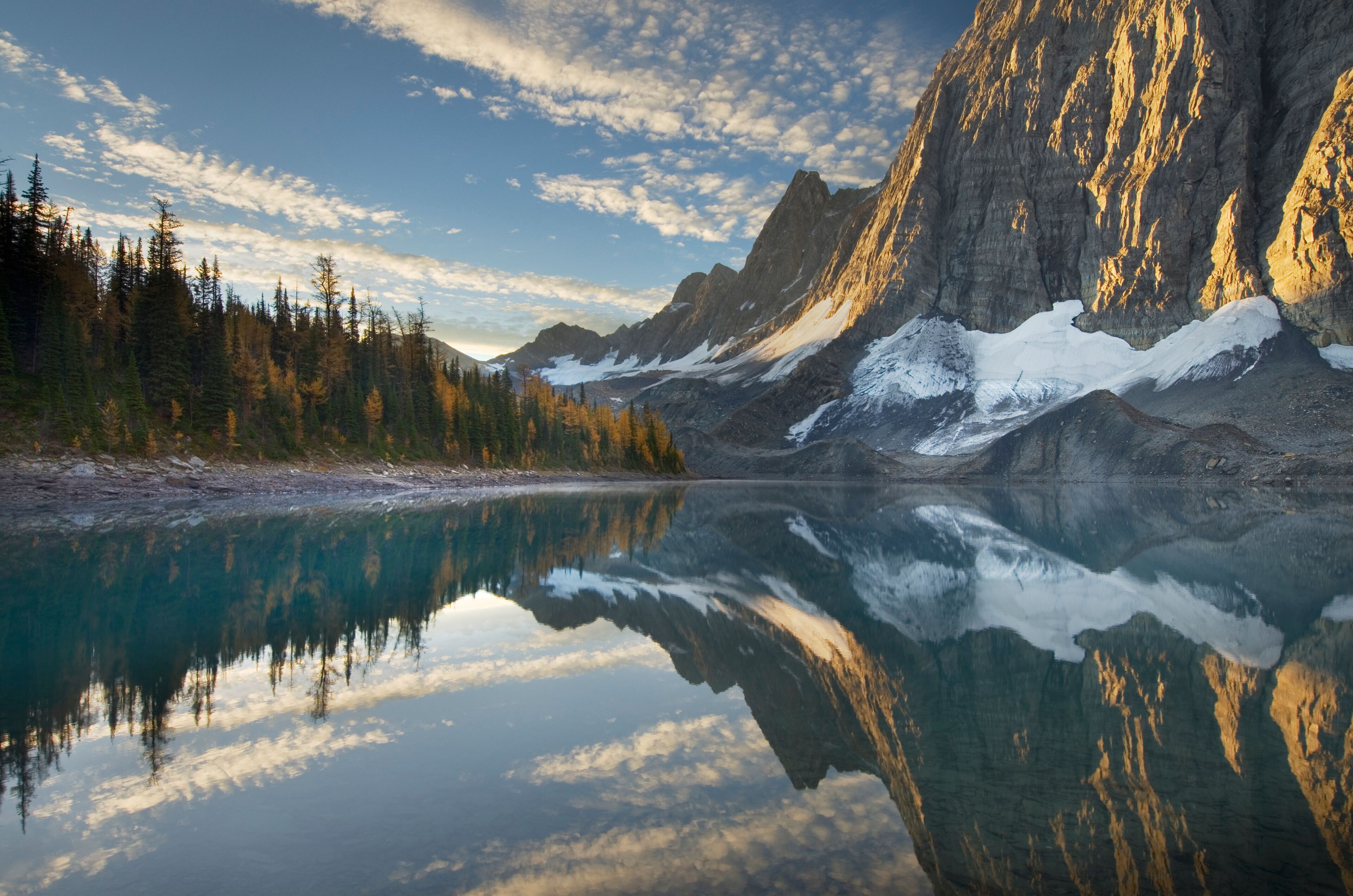 A mountain lake with reflections, snow-capped peaks, and a forested valley.