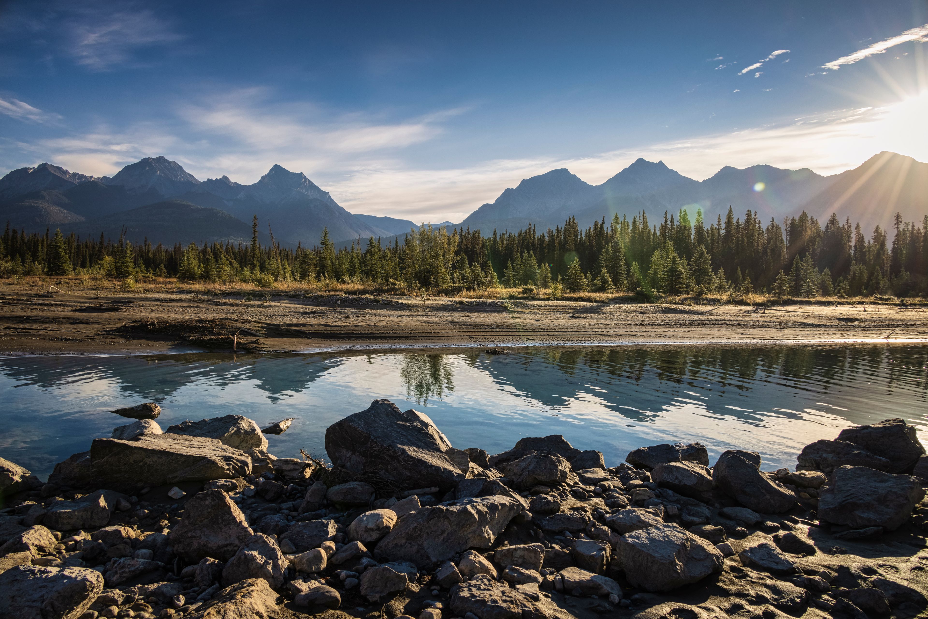 A mountain landscape with a calm river reflecting the trees and mountains.