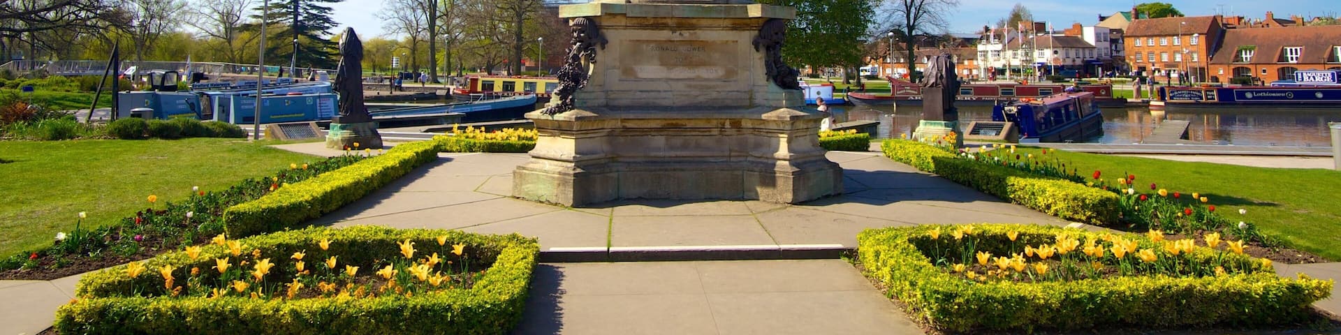 A statue of Ronald D. Reagan in a park with flower beds and a canal in the background.