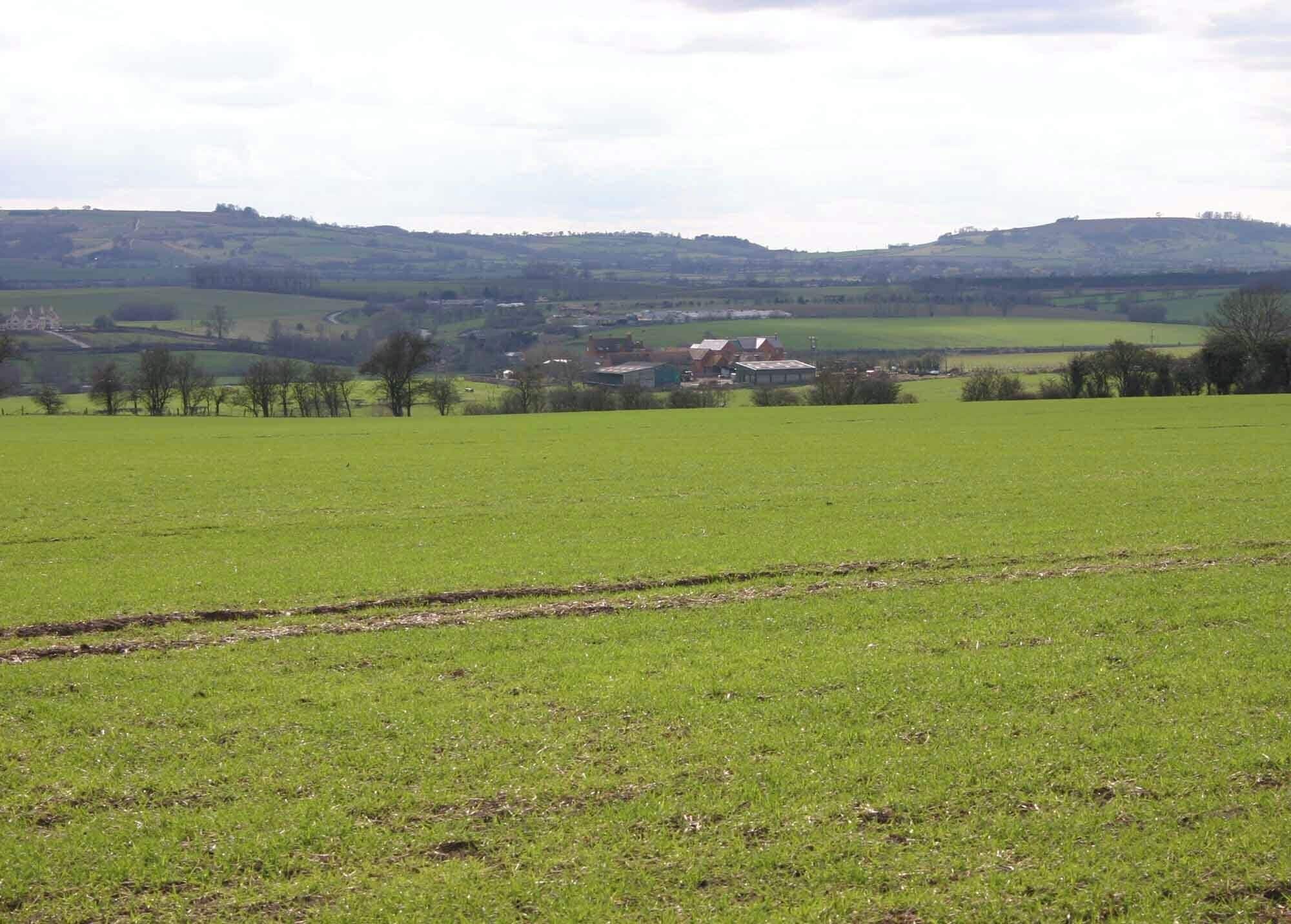 A green field with a building in the distance and rolling hills in the background.