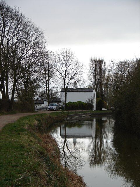 A calm canal with a white house and trees in the background.
