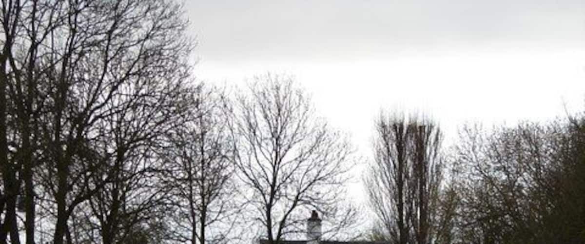 A calm canal with a white house and trees in the background.