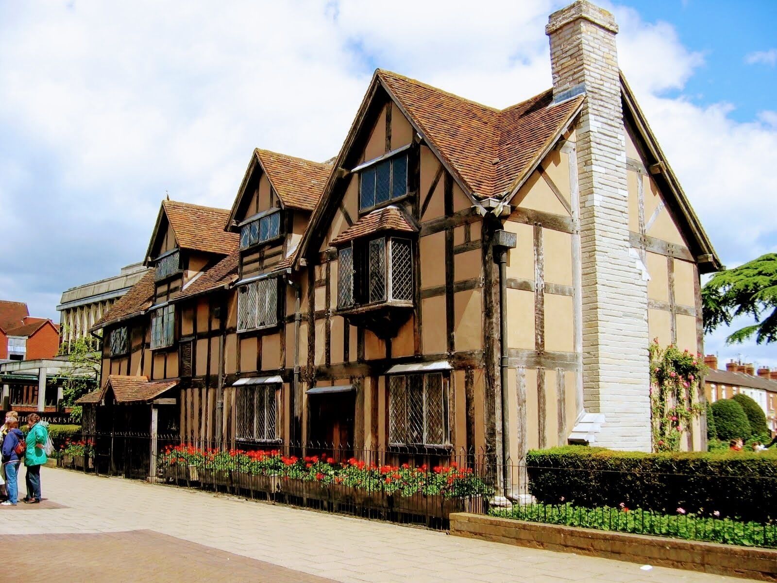 A Tudor-style building with a stone chimney, wooden beams, and a flower bed in front.