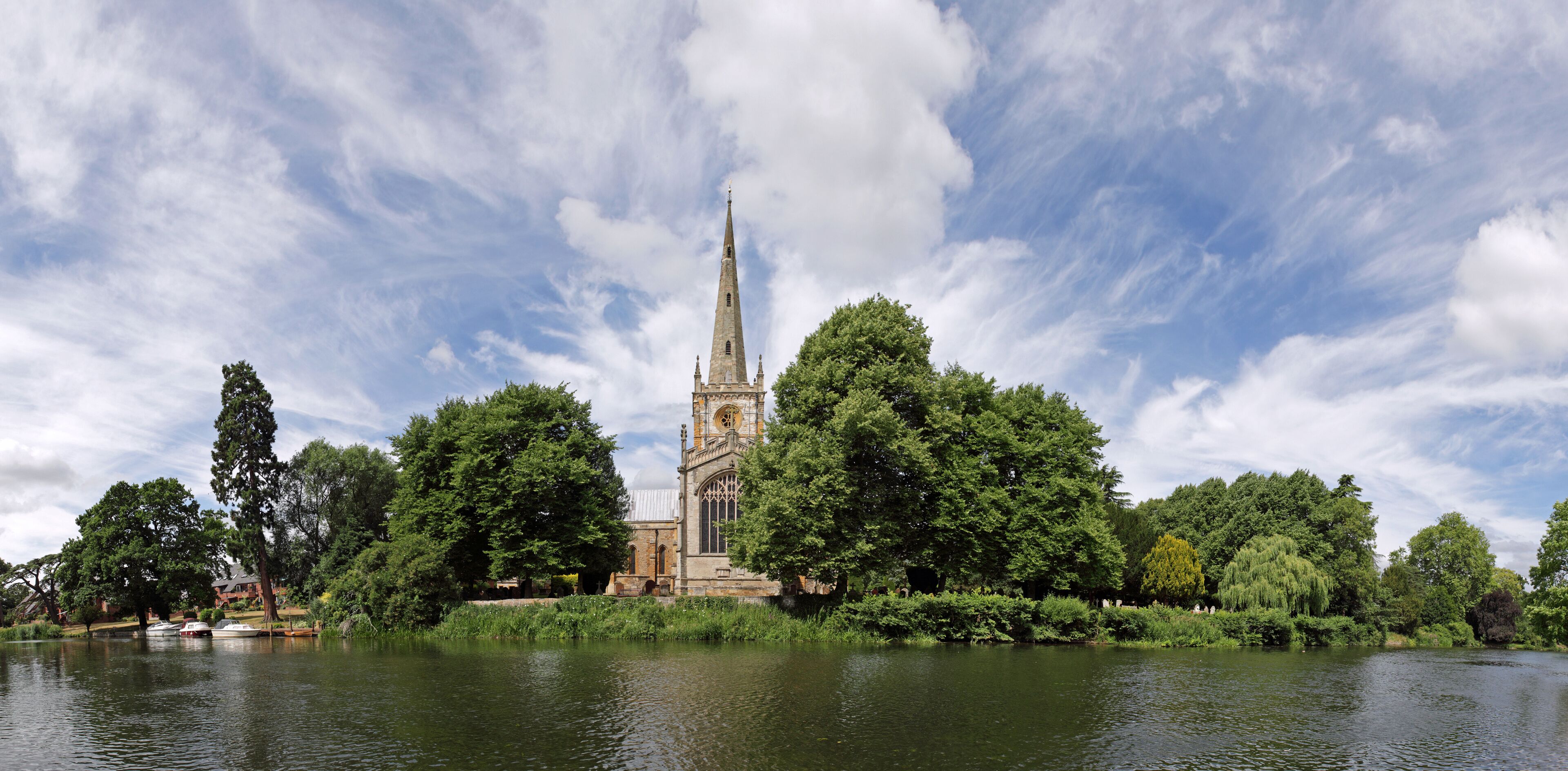 A church with a tall spire surrounded by lush greenery and a calm lake.
