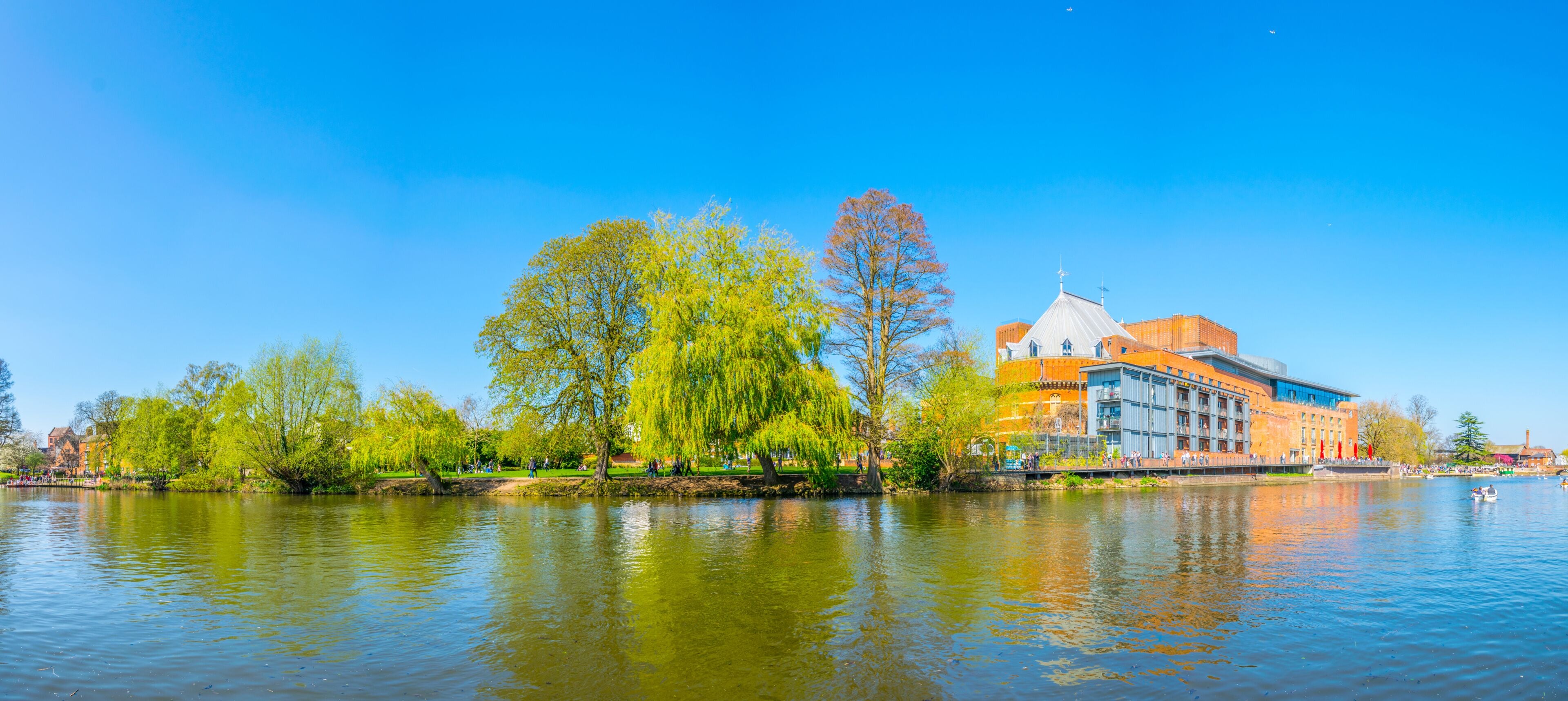 A river with a park, trees, and a building with a dome and cross.