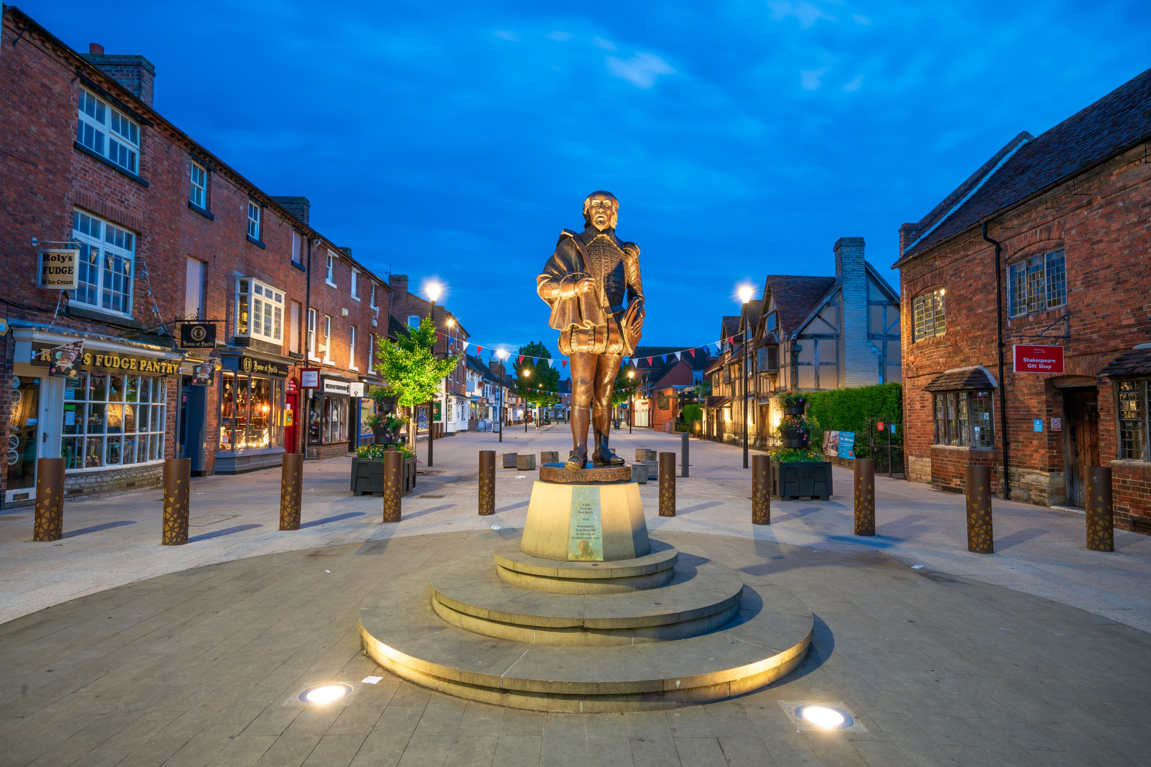 A statue in a town square with brick buildings and shops around.