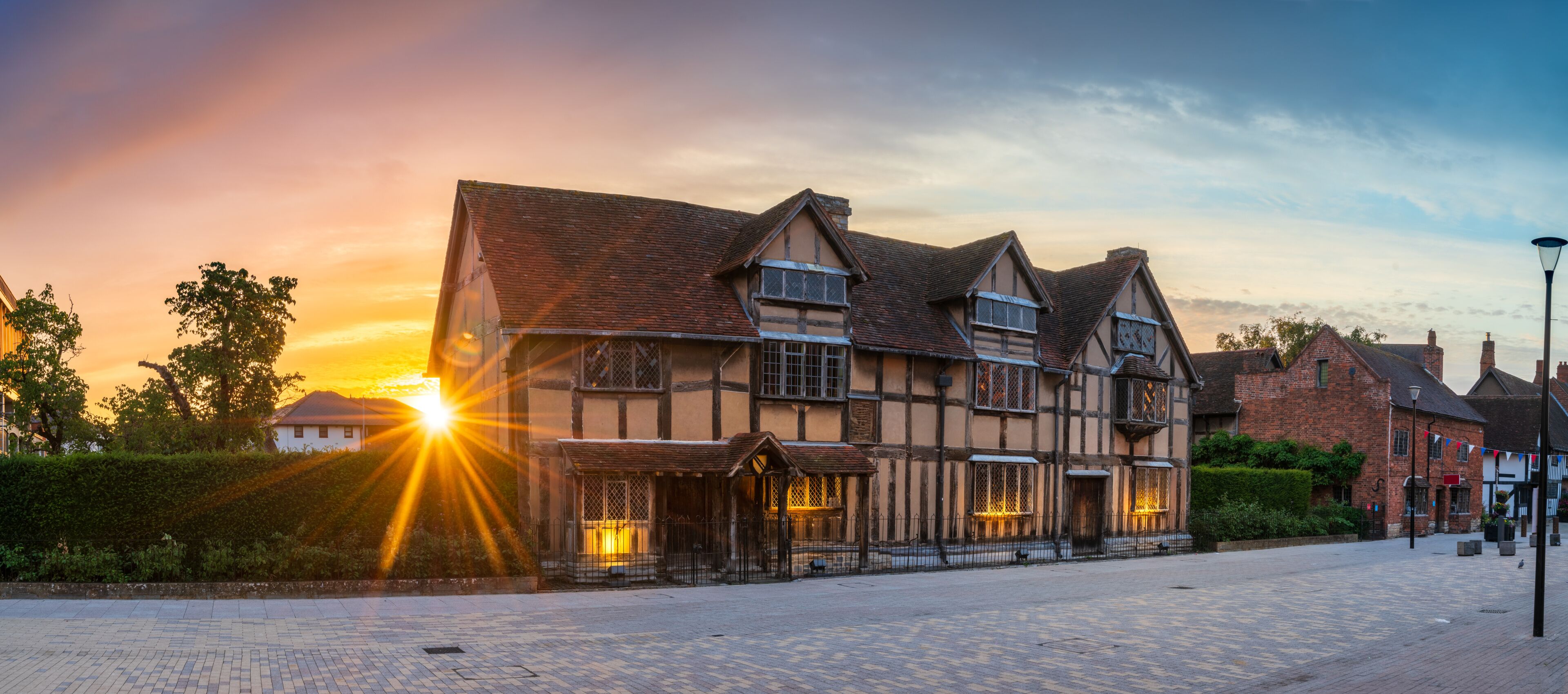 A historic half-timbered building with a tiled roof, surrounded by cobblestone pavement and greenery.
