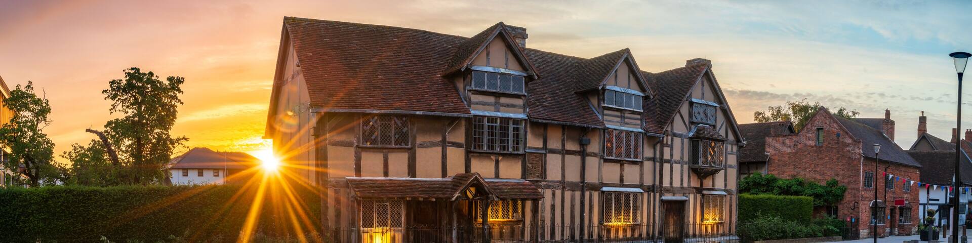 A historic half-timbered building with a tiled roof, surrounded by cobblestone pavement and greenery.