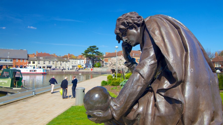 A bronze statue of a man holding a globe, with a canal and boats in the background.