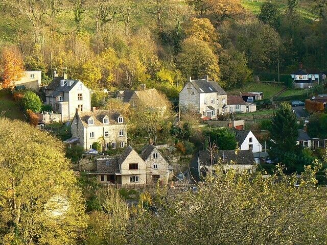 A village with stone houses surrounded by trees and hills.