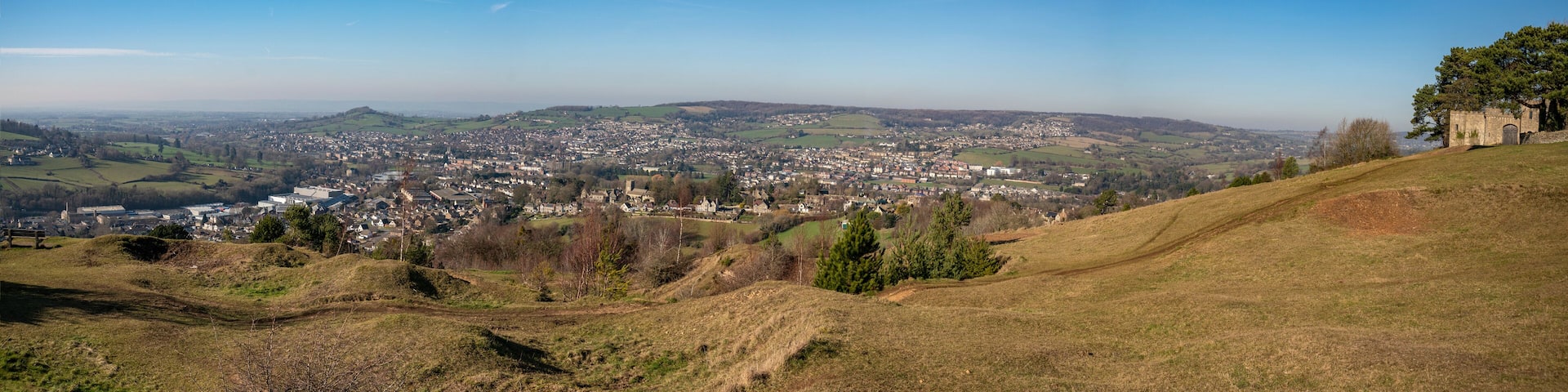 A panoramic view of a town nestled in a valley, surrounded by rolling hills and a clear blue sky.