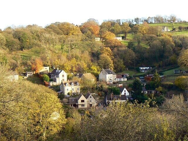 A village nestled in a valley with houses surrounded by autumn foliage and rolling hills.