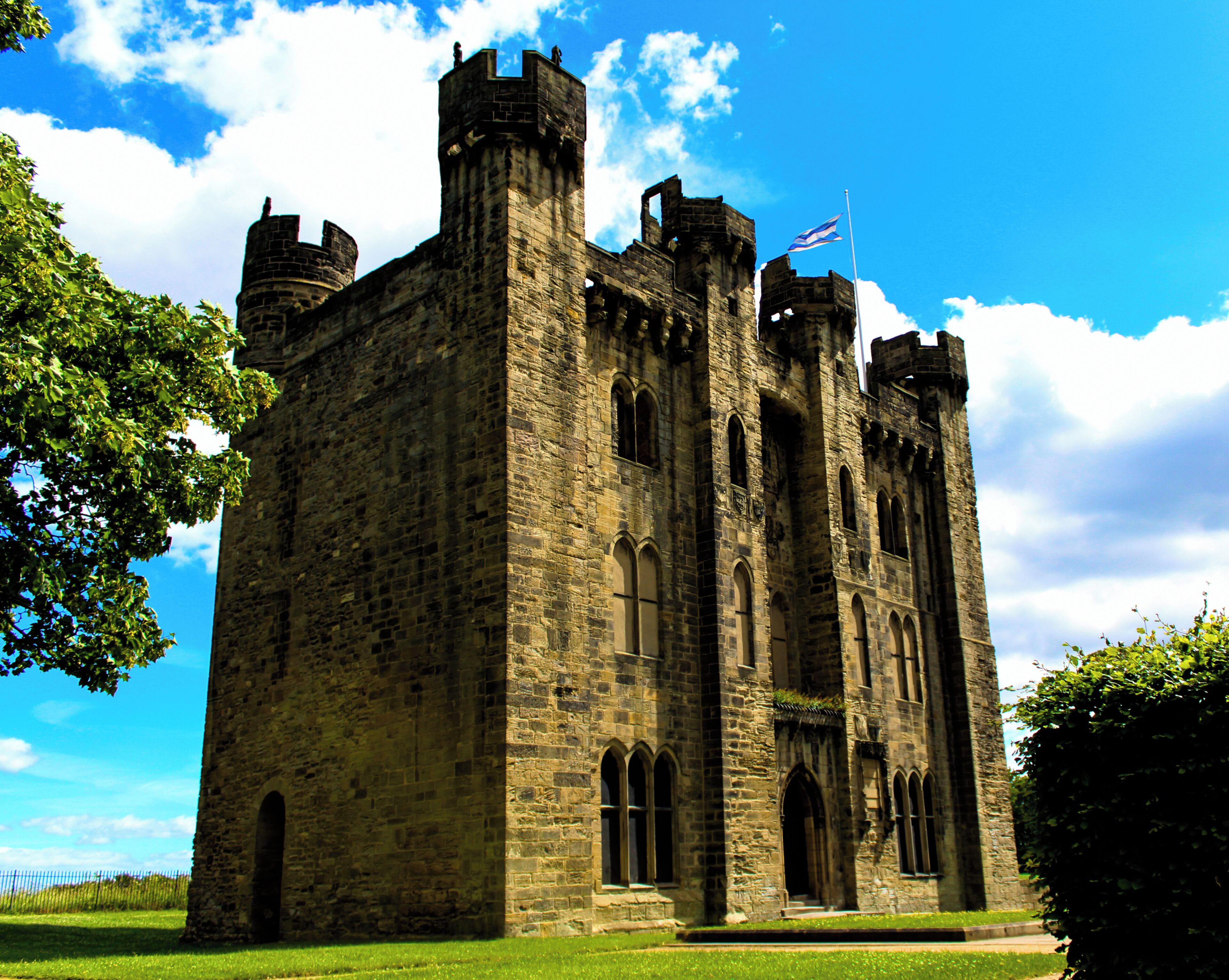 A historic stone castle with multiple towers and arched windows, surrounded by lush green grass and trees.