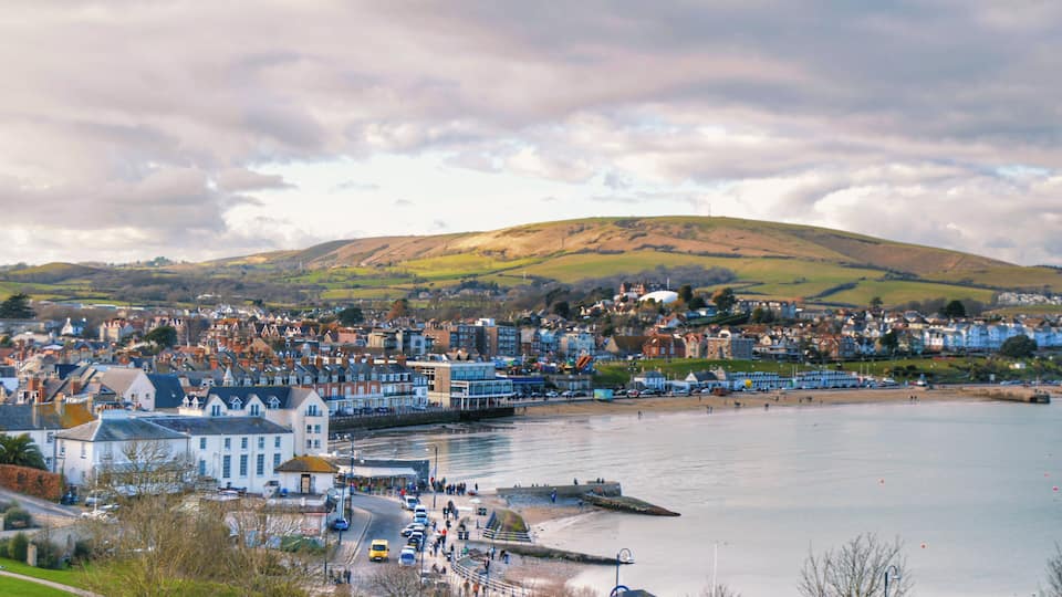 A coastal town with a beach, a hill in the background, and a mix of residential and commercial buildings.
