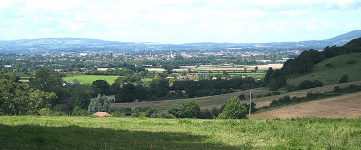 A rural landscape with rolling hills, fields, and a distant town.