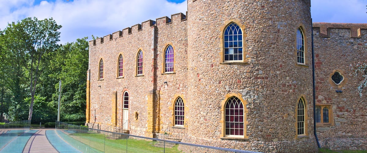 Taunton castle, Somerset Museum, England, Uk. Bright summer morning with blue sky and some clouds, green meadow and trees, glazed walkway