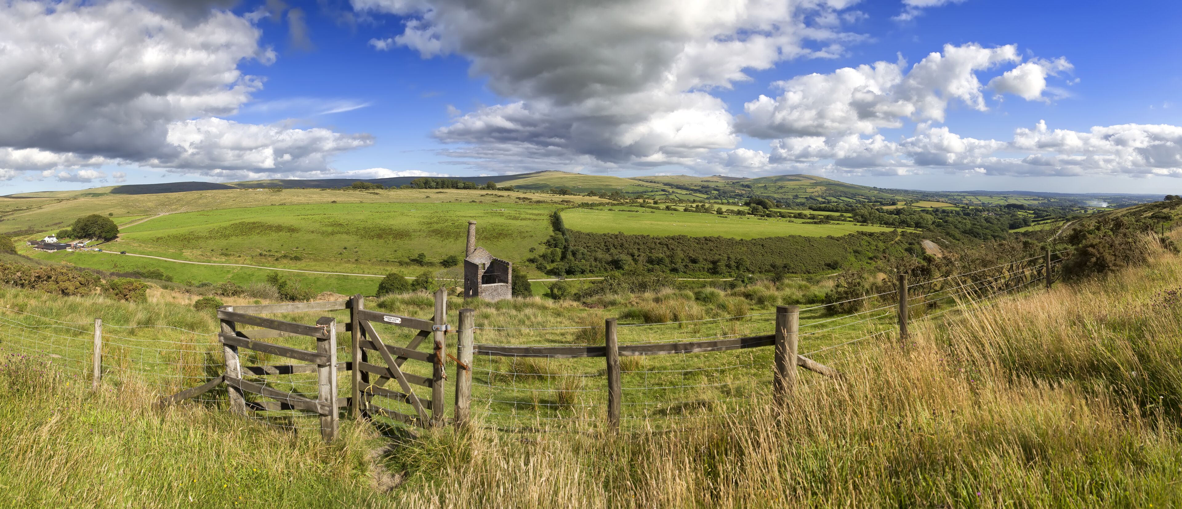 A rural landscape with rolling hills, a stone structure, and a fenced area.