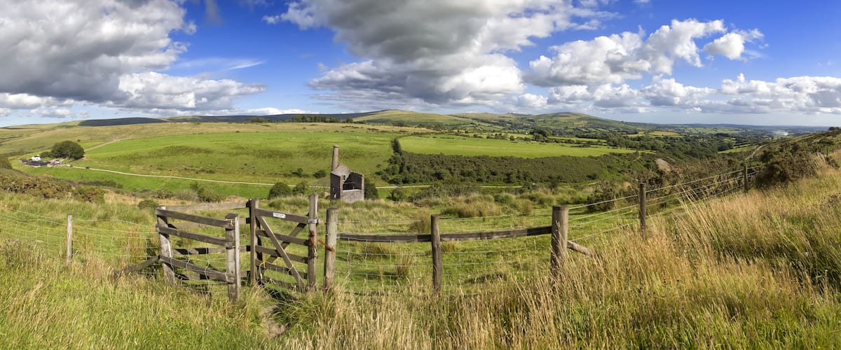 A rural landscape with rolling hills, a stone structure, and a fenced area.