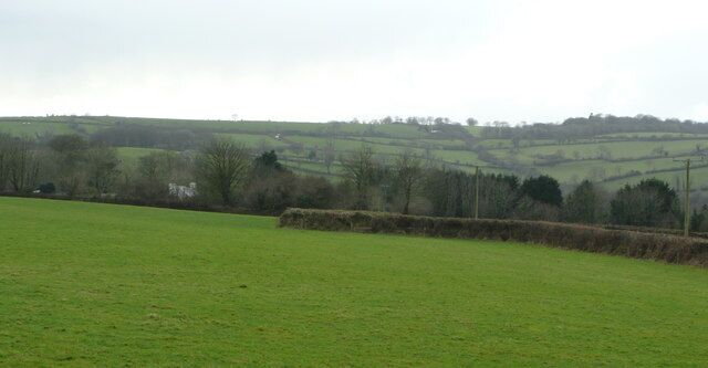 A green field with a stone wall and a distant view of rolling hills and a white building.