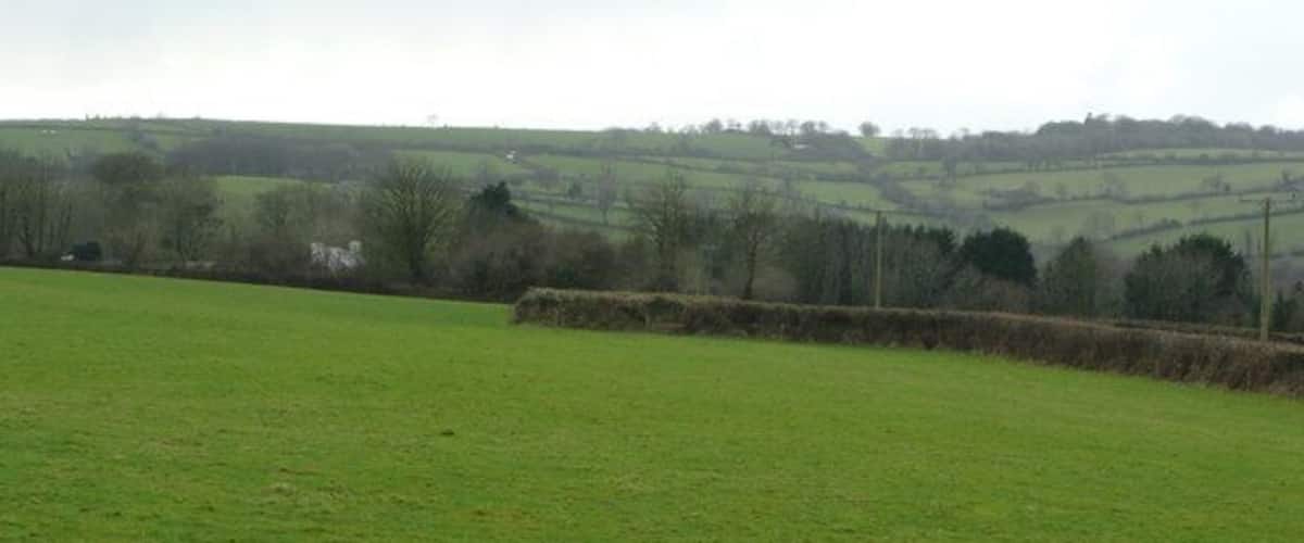A green field with a stone wall and a distant view of rolling hills and a white building.