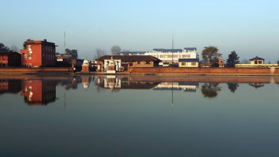 A calm river reflecting buildings and a clear sky.