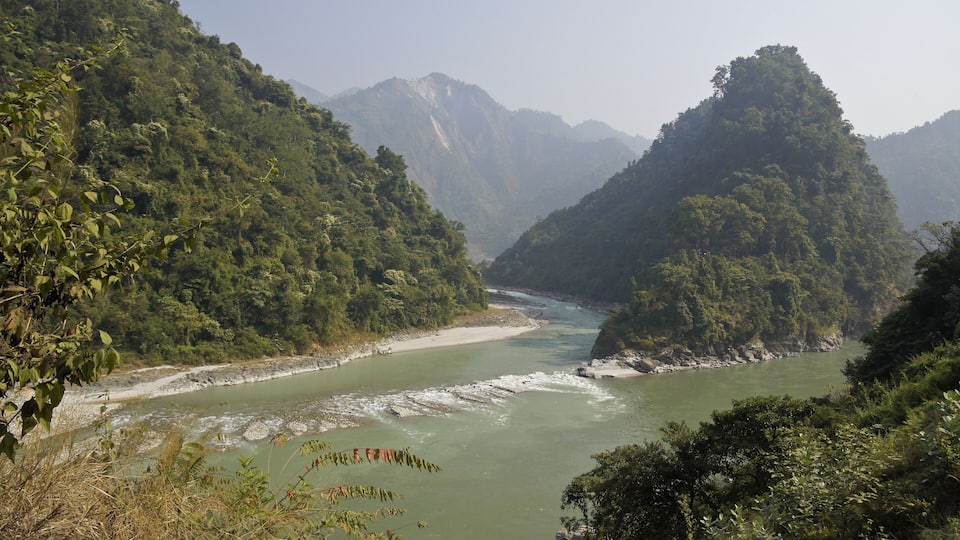 A river winding through a mountainous landscape with dense greenery and rocky riverbanks.