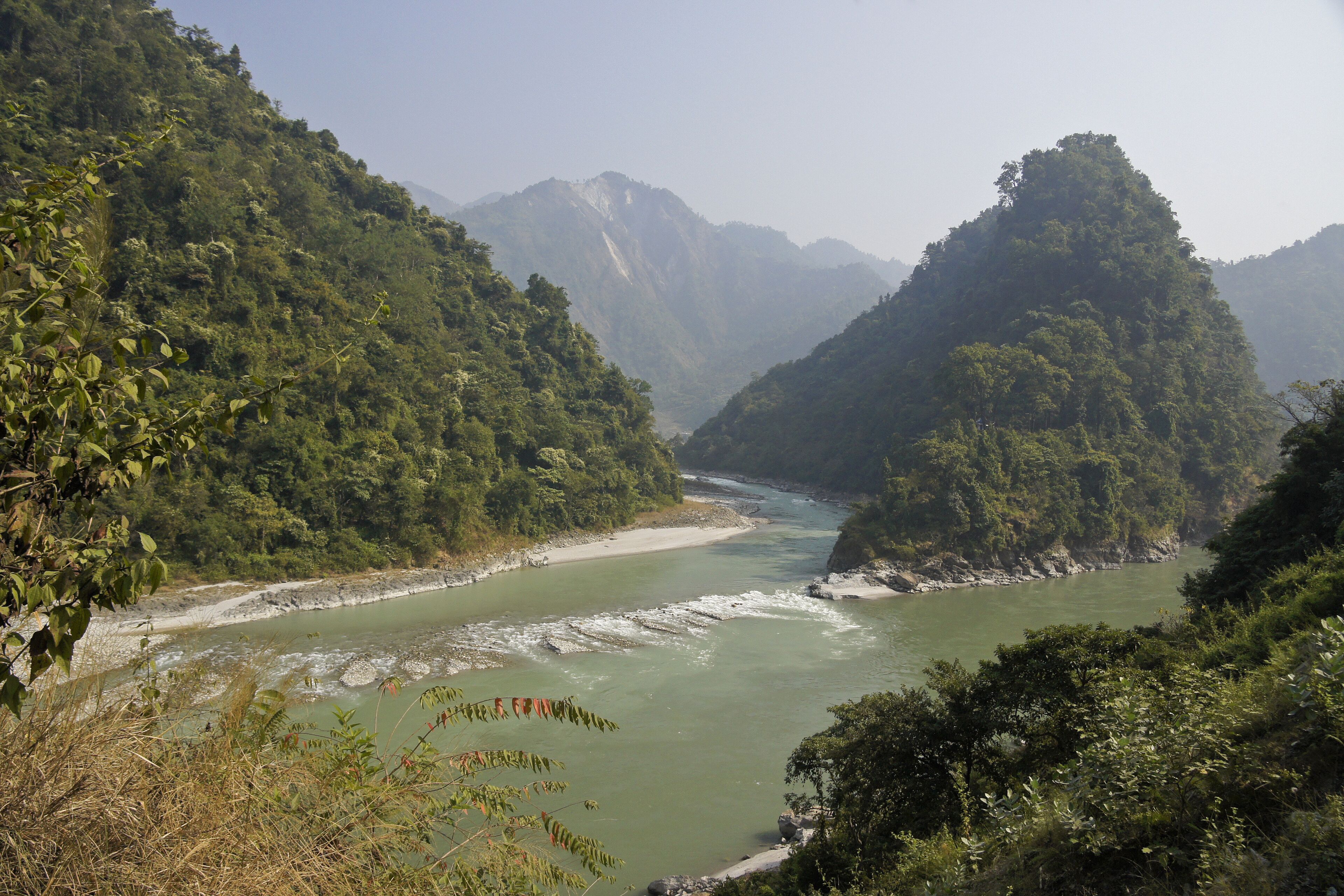 A river winding through a mountainous landscape with dense greenery and rocky riverbanks.