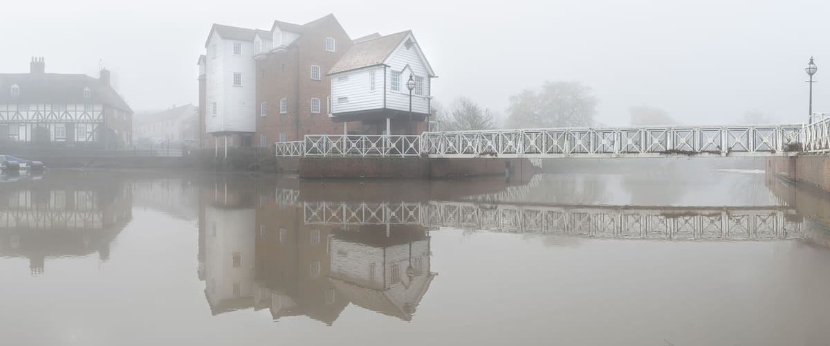 A foggy river with buildings reflected on the water.