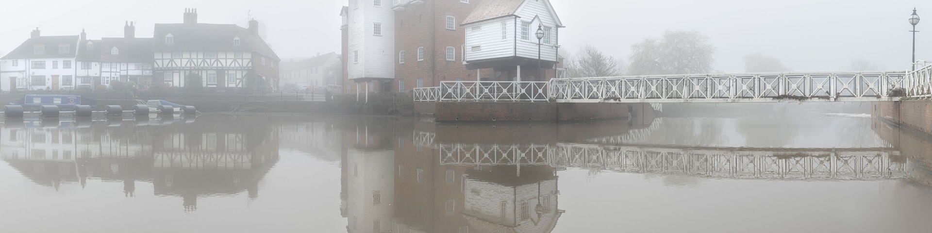 A foggy river with buildings reflected on the water.