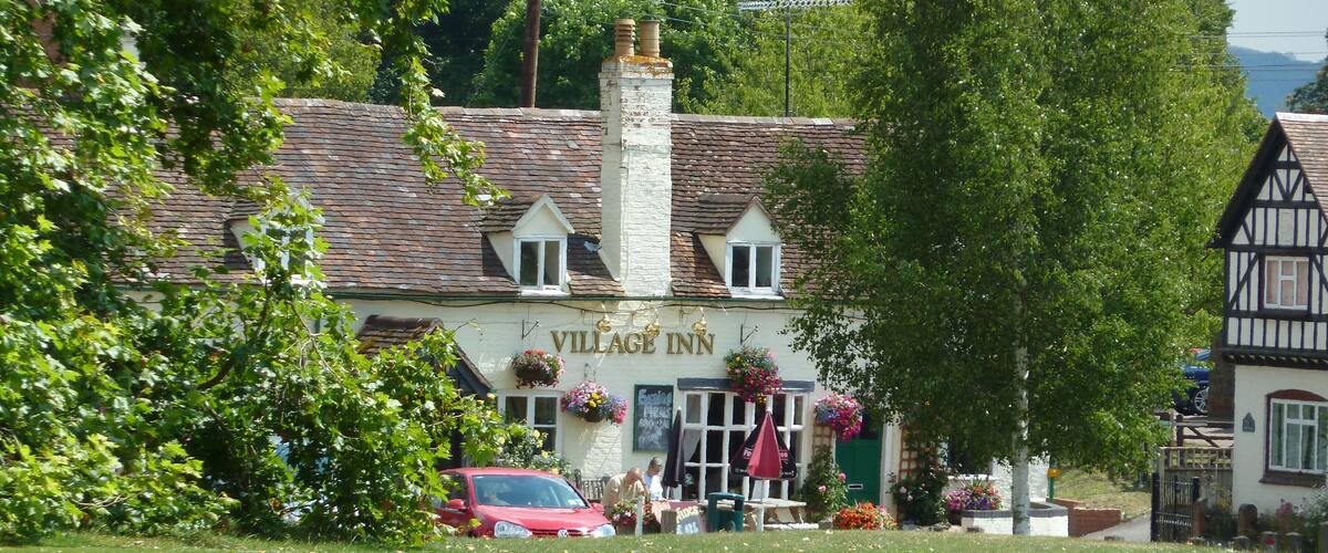 A traditional building with a sign reading "VILLAGE INN" surrounded by lush greenery and a red car parked in front.