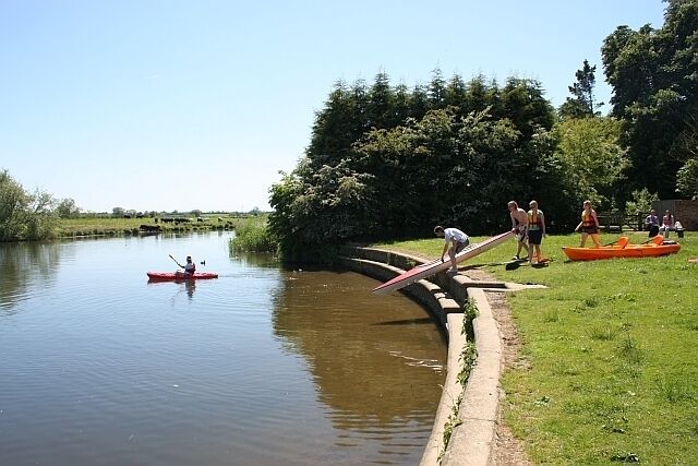 Un río tranquilo con una persona en kayak, un puente y gente de pie en la orilla.
