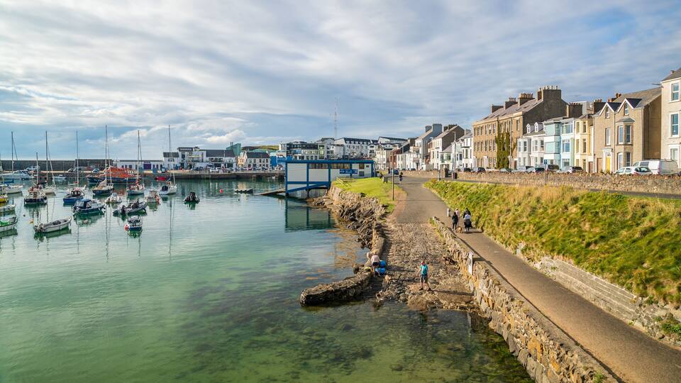 A coastal town with a harbor filled with boats, a stone wall, and colorful houses along the shore.